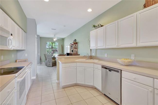 Kitchen featuring white appliances, a kitchen breakfast bar, white cabinetry, a peninsula, and recessed lighting and a desk area | Image 21
