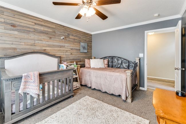 Carpeted bedroom with wooden walls, crown molding, a ceiling fan, and baseboards | Image 24
