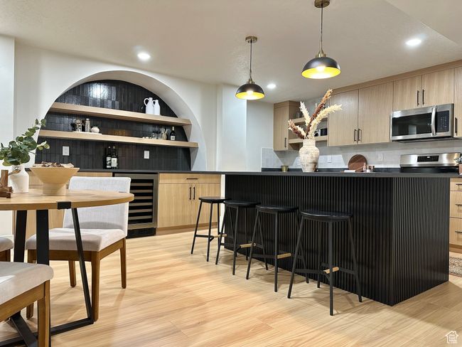 Indoor bar with stainless steel microwave, beverage cooler, decorative backsplash, light wood-style flooring, and decorative light fixtures | Image 27
