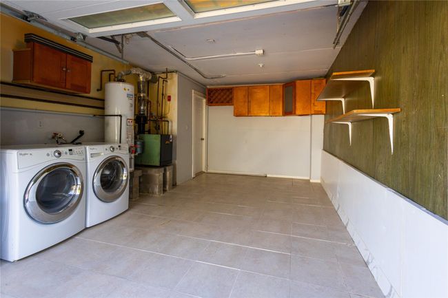 Garage featuring laundry area with water heater, independent washer and dryer, and wood clad walls | Image 23
