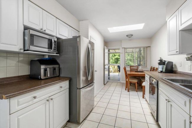 Kitchen with a skylight, light tile patterned flooring, stainless steel appliances, decorative backsplash, and dark countertops | Image 12