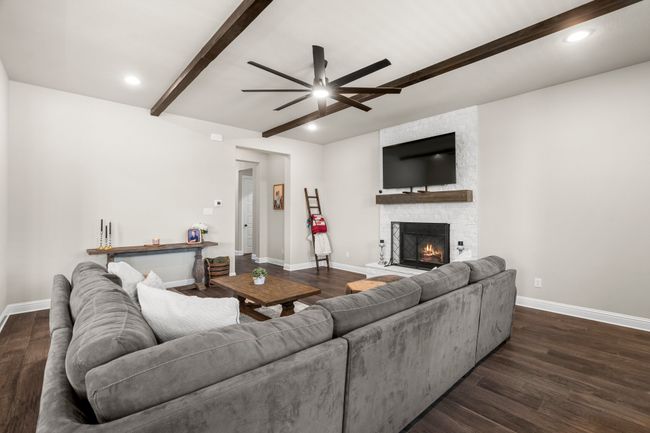 Living area with beam ceiling, a ceiling fan, a stone fireplace, dark wood finished floors, and recessed lighting | Image 7