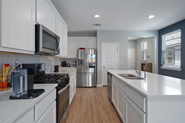 Kitchen with stainless steel appliances, tasteful backsplash, white cabinets, light wood-type flooring, and an island with sink | Image 5