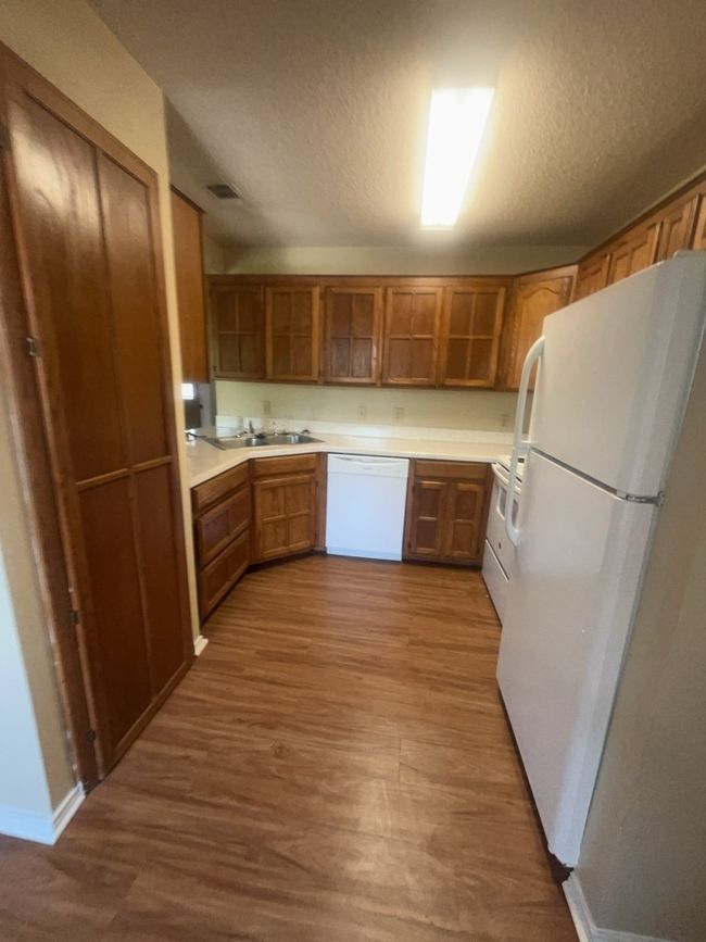 Kitchen with white appliances, open shelves, wood finished floors, brown cabinetry, and a textured ceiling | Image 6