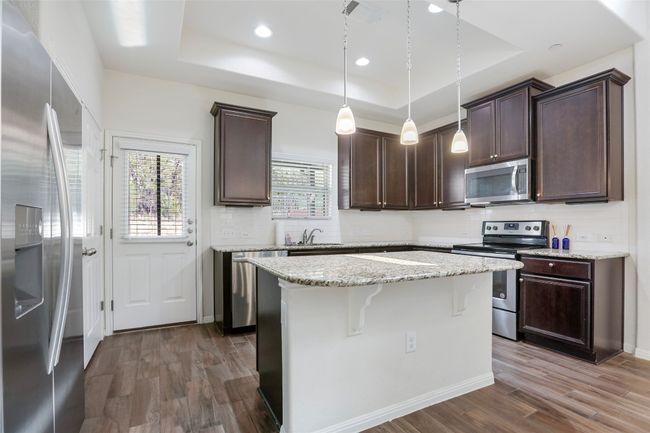 Kitchen featuring dark brown cabinetry, appliances with stainless steel finishes, a sink, and a raised ceiling | Image 7