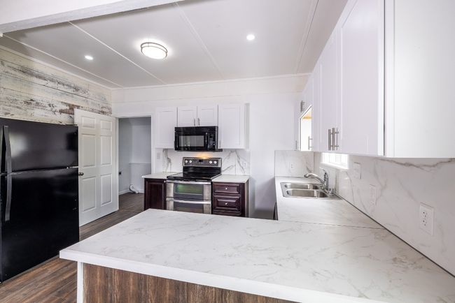 Kitchen featuring dark wood-style flooring, a peninsula, white cabinets, black appliances, and a sink | Image 9