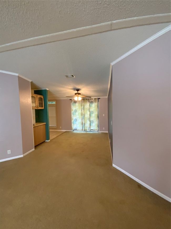 Unfurnished living room featuring crown molding, ceiling fan, light colored carpet, baseboards, and visible vents | Image 12