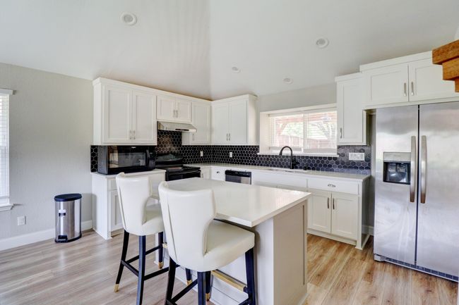 Kitchen with black appliances, under cabinet range hood, light wood-type flooring, and tasteful backsplash | Image 10