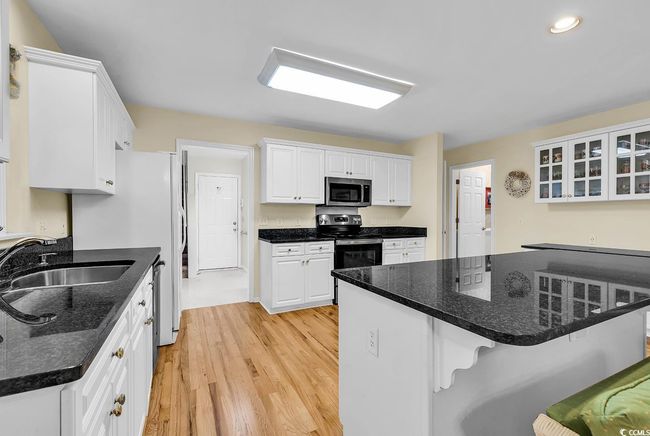 Kitchen featuring appliances with stainless steel finishes, a kitchen bar, light wood-style floors, white cabinetry, and glass insert cabinets | Image 22