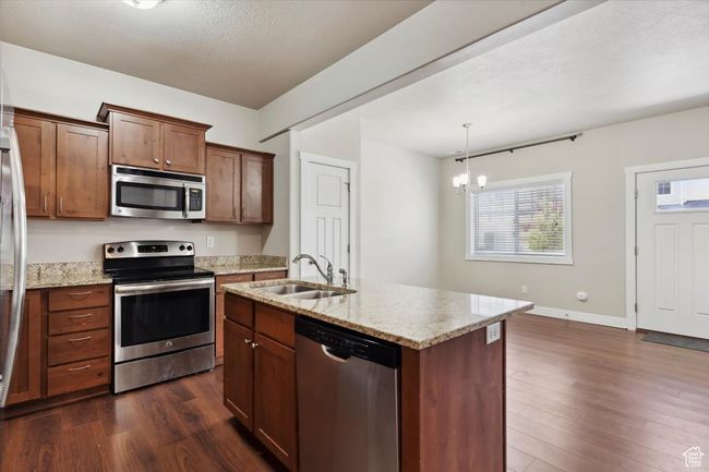Kitchen featuring stainless steel appliances, dark wood-style floors, a sink, a chandelier, and light stone countertops | Image 11