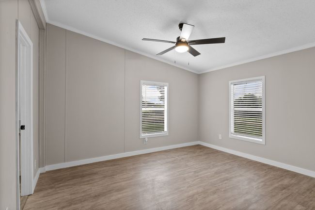 Spare room with crown molding, light wood-type flooring, healthy amount of natural light, lofted ceiling, and ceiling fan | Image 22