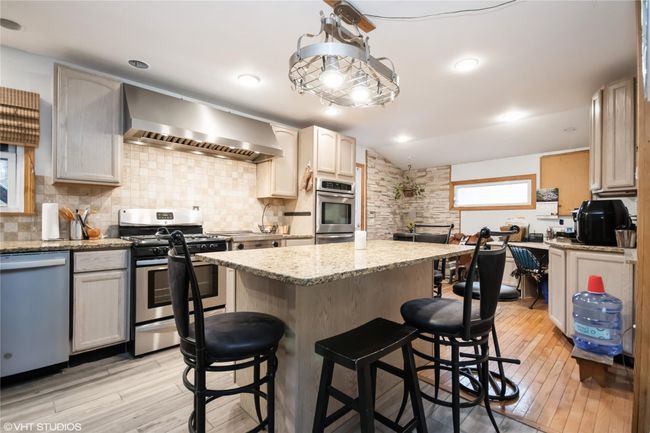 Kitchen featuring a breakfast bar area, wall chimney exhaust hood, a center island, stainless steel appliances, and decorative backsplash | Image 12