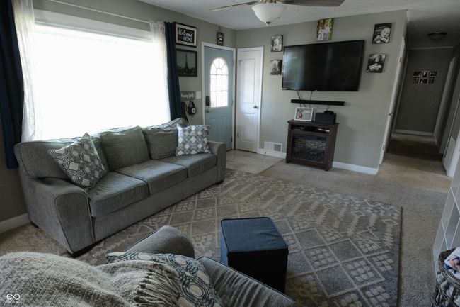 carpeted living area featuring baseboards, visible vents, a fireplace, and ceiling fan | Image 12