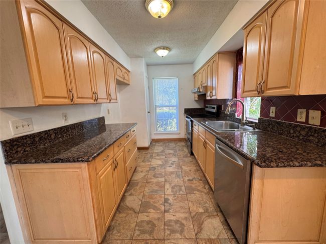 Kitchen with appliances with stainless steel finishes, a textured ceiling, decorative backsplash, dark stone countertops, and light brown cabinetry | Image 4