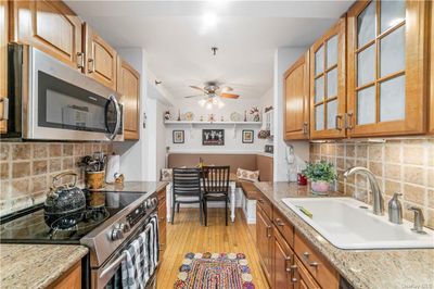 Kitchen featuring backsplash, light hardwood / wood-style floors, stainless steel appliances, sink, and ceiling fan | Image 1