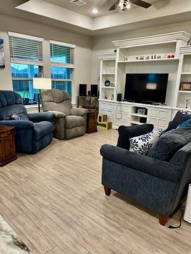 Experience a welcoming hallway with sleek wood-look tile flooring leading to a cozy living area. Enjoy abundant natural light and large windows that enhance the spacious feel. | Image 5