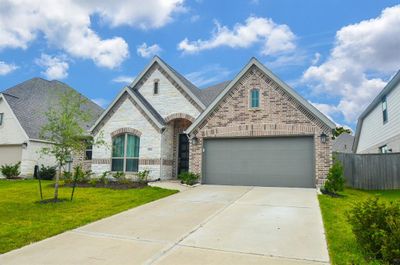 The photo showcases a modern single-story brick home with an arched entryway, a two-car garage, and a well-maintained lawn. | Image 2