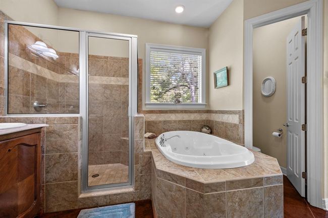 Corner-mounted jetted soaking tub beside a walk-in shower, all wrapped in premium tile for a true spa experience. | Image 27