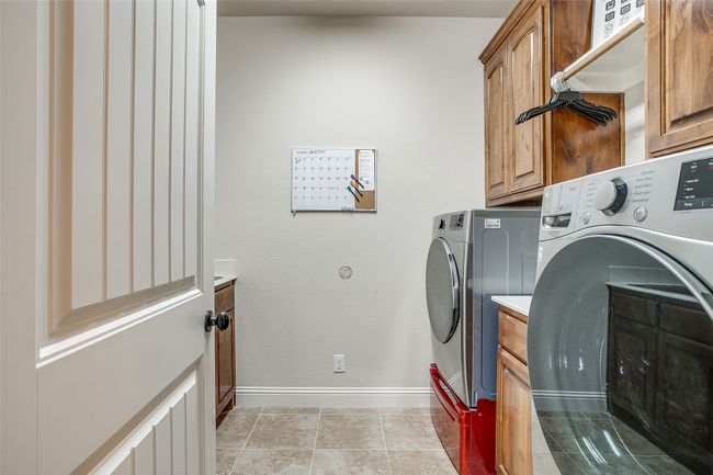 Clothes washing area with washer and dryer, light tile patterned floors, baseboards, and cabinet space | Image 25