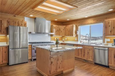 Kitchen with appliances with stainless steel finishes, light wood-type flooring, a center island, sink, and wall chimney range hood | Image 3