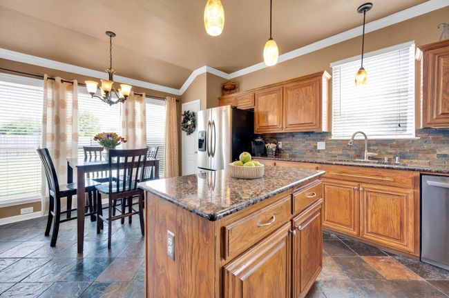 Kitchen with stainless steel appliances, stone tile flooring, healthy amount of natural light, brown cabinetry, and ornamental molding | Image 16