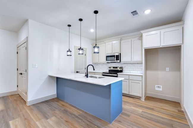 Kitchen featuring light wood-type flooring, a peninsula, visible vents, appliances with stainless steel finishes, and a sink | Image 4
