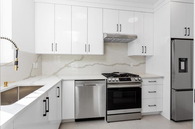 Kitchen featuring under cabinet range hood, light stone counters, a sink, appliances with stainless steel finishes, and white cabinets | Image 12