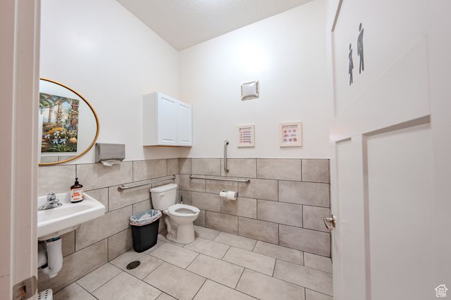Bathroom featuring tile walls, tile patterned flooring, vaulted ceiling, a wainscoted wall, and toilet | Image 7