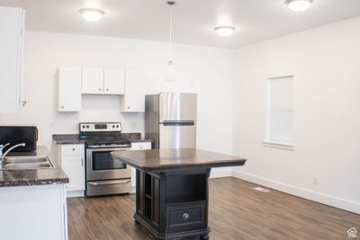 Kitchen featuring hanging light fixtures, dark hardwood / wood-style flooring, white cabinetry, sink, and stainless steel appliances | Image 3