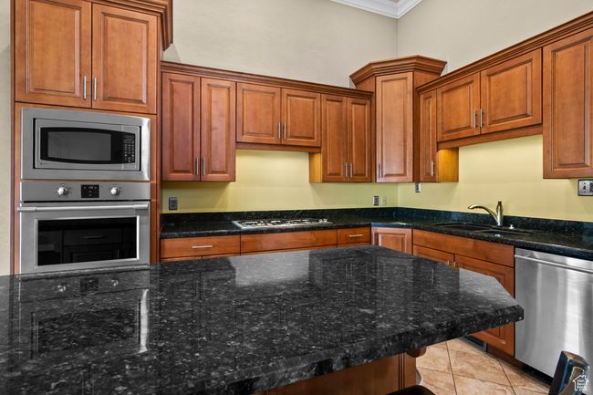Kitchen with appliances with stainless steel finishes, ornamental molding, dark stone countertops, light tile patterned floors, and brown cabinetry | Image 18