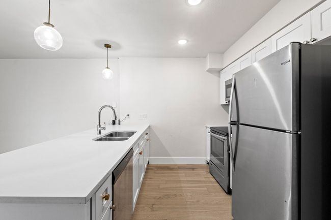 Kitchen featuring stainless steel appliances, a sink, a peninsula, light wood finished floors, and light countertops | Image 12