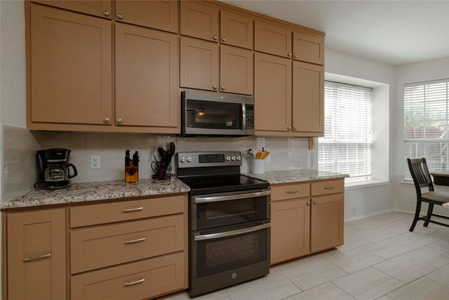 Kitchen featuring decorative backsplash, baseboards, light stone counters, and appliances with stainless steel finishes | Image 15