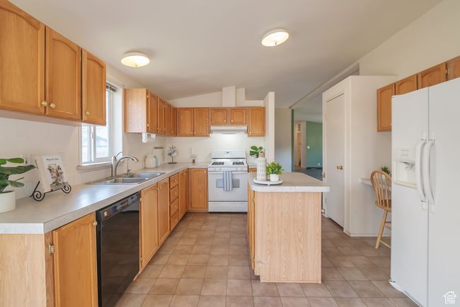 Kitchen featuring white appliances, a sink, light countertops, lofted ceiling, and a center island | Image 4