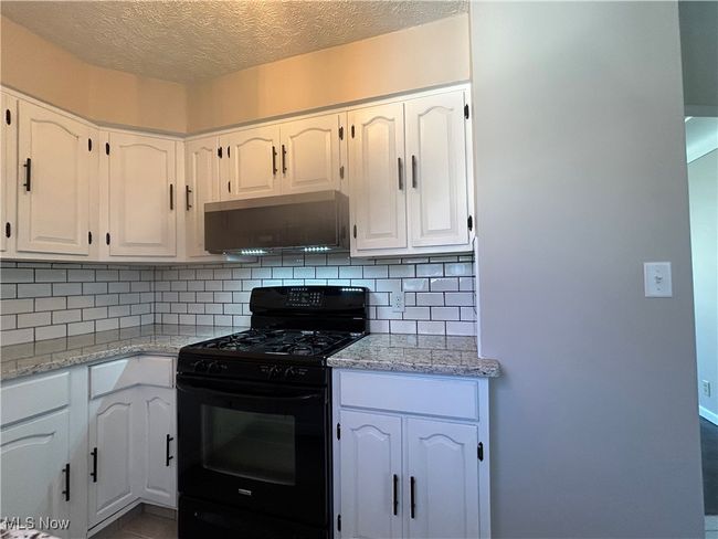 Kitchen featuring decorative backsplash, black gas stove, new microwave and white cabinetry. | Image 9
