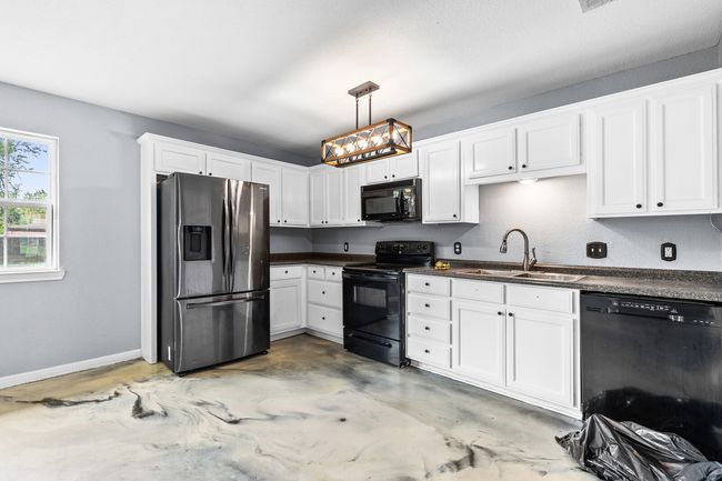 Kitchen with black appliances, dark countertops, white cabinetry, hanging light fixtures, and concrete floors | Image 19