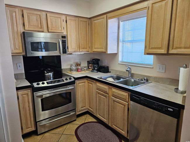 Kitchen featuring stainless steel appliances, light tile patterned flooring, light brown cabinetry, and light countertops | Image 10