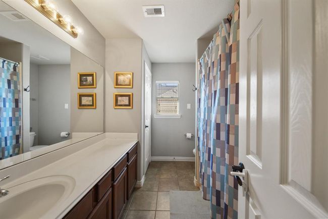 Conveniently located near the second & third bedrooms is the home's second full bath. Features include a wood-stained cabinet with a solid surface counter top and integrated back splash, wall mounted mirror & lighting, a ceramic tile surrounded combination tub/shower, linen closet, a window with blinds & tile flooring. An additional linen closet is located in the corridor. | Image 32
