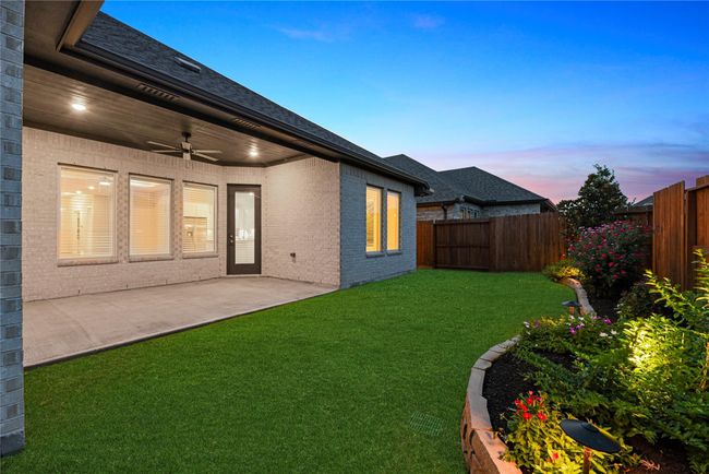 At twilight, this charming backyard offers a serene escape with a covered patio, blooming flowers, and the combination of soft glow of interior lights and exterior landscape lighting creating the perfect setting for quiet evenings or relaxed outdoor gatherings. | Image 36