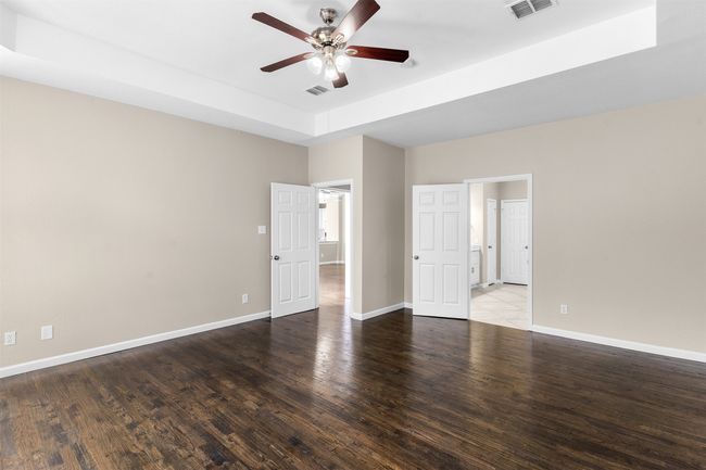 Unfurnished bedroom with baseboards, a tray ceiling, visible vents, and wood finished floors | Image 21