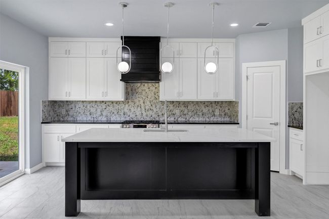Kitchen with backsplash, light stone counters, ventilation hood, a kitchen island with sink, and decorative light fixtures | Image 12
