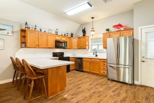 This bright kitchen features cabinets, modern stainless steel finish appliances, and a large island with bar seating. The flooring adds warmth, and spacious counter space makes it ideal for cooking and entertaining. | Image 9