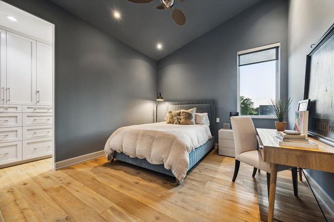 Another well-proportioned secondary bedroom showcases serene tones, soaring ceilings, and natural wood floors. The large window fills the space with light, with room for a desk area offering a functional study or work-from-home nook. Custom cabinetry provides generous storage, continuing the home’s theme of smart, stylish design. | Image 34
