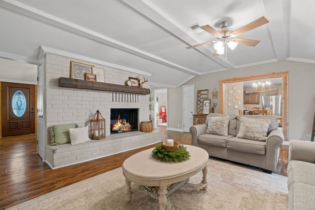 Living room featuring ceiling fan, wood finished floors, a brick fireplace, and ornamental molding | Image 22