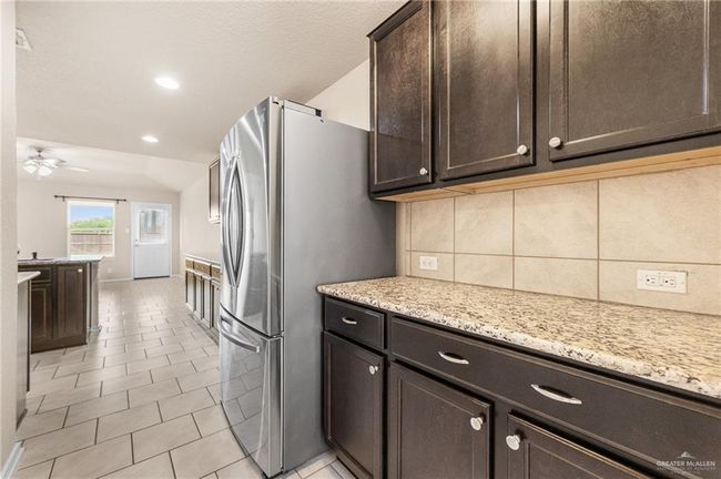 Kitchen with freestanding refrigerator, dark brown cabinets, decorative backsplash, a ceiling fan, and light stone countertops | Image 4