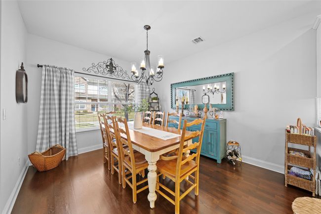 Dining space with dark wood-style floors, a notable chandelier, visible vents, and baseboards | Image 5