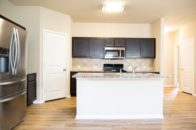 Kitchen featuring stainless steel appliances, light wood finished floors, decorative backsplash, and light stone counters | Image 6