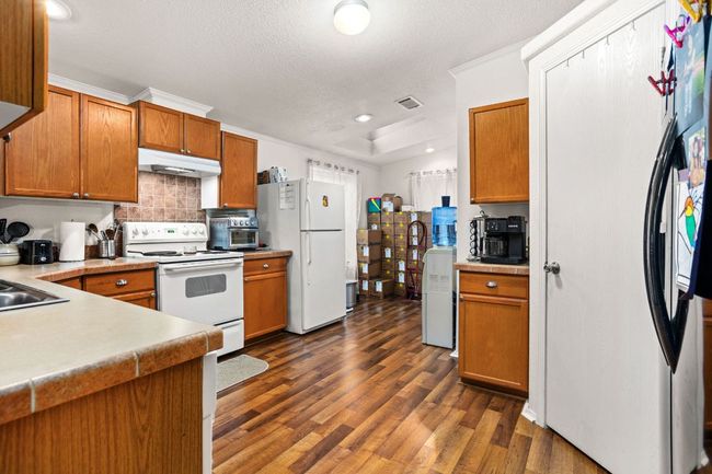 Kitchen with decorative backsplash, dark wood-style flooring, white appliances, under cabinet range hood, and brown cabinetry | Image 14