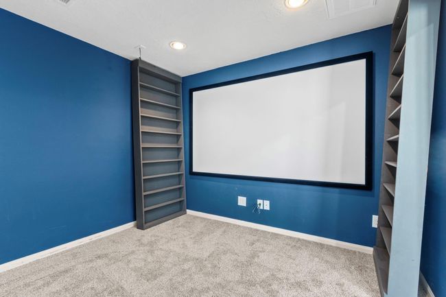 This room features a cozy home theater setup with blue walls, recessed lighting, and built-in shelving. Ideal for entertainment, it includes a large screen and plush carpeting for comfort. | Image 21