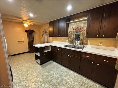 Kitchen with kitchen peninsula, sink, ceiling fan, dark brown cabinetry, and light tile floors | Image 3