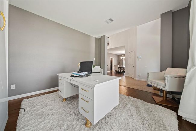 Located just off the foyer, this spacious home office features rich wood flooring, soothing neutral tones, and a wide front-facing window that fills the room with natural light. | Image 9
